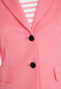 Pink blazer with a notched lapel, two black buttons, and side pockets, layered over a white and pink striped top. Smooth texture.