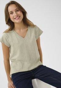 Ljust grön, kortärmad V-ringad T-shirt med avslappnad passform, tillverkad av mjukt material; bärs med mörkblå jeans.