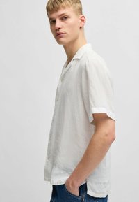 Korte mouwen witte linnen shirt met een knoopsluiting ontwerp, subtiele textuur en een ontspannen pasvorm. De onderkant is iets gebogen.