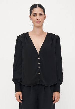 Blusa negra que presenta mangas largas, un escote en V profundo, hombros con pliegues y detalles de botones decorativos en el frente. Textura de tela suave.