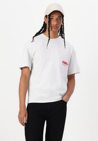 Light gray short-sleeve t-shirt with a red "POMI" logo on the chest, paired with black pants and a beige cap. Smooth texture.