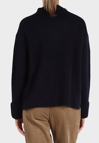 Maglione rigato blu navy con collo alto e spalle ribassate, caratterizzato da un tessuto texturizzato e maniche ripiegate, abbinato a pantaloni in corduroy beige.
