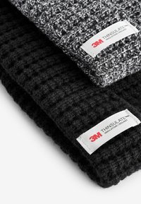 Due pezzi di tessuto lavorato a maglia: uno grigio con un motivo testurizzato, l'altro in nero uniforme, entrambi con etichette "3M THINSULATE".