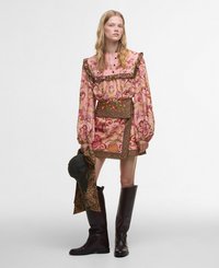 Rochie florală multicoloră cu mâneci lungi, guler fronsat și curea cu model. Asortată cu cizme maro până la genunchi și o pălărie verde.