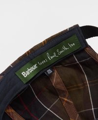 Boné Barbour com um rótulo verde com "também ama Paul Smith", contra um padrão xadrez nas cores castanho, burgundy e creme. Tag com tamanho visível.