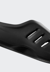 Detailní záběr na černou texturovanou nazouvací sandálovou obuv se třemi horizontálními ventilačními štěrbinami a tvarovanou stélkou.