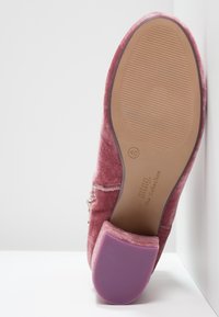 Zapato plano de terciopelo rosa visto desde la suela con la talla 40 marcada, suela marrón texturizada, tacón púrpura y cremallera lateral visible.
