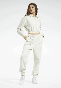 Cremfarbener Athleisure-Set bestehend aus einem gekürzten Pullover mit Kragen und tapered Jogginghosen mit elastischen Bündchen. Strukturierter, weicher Stoff.