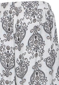 Tissu blanc avec broderie noire paisley et florale formant des motifs ornementaux répétitifs et complexes.