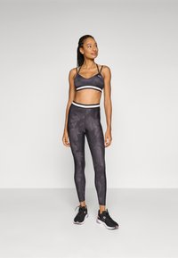 Sötét szürke sport melltartó és leggings, kamuflázs mintával, fehér díszcsíkokkal és feszes szabással. Fekete sportcipők rózsaszín részletekkel.