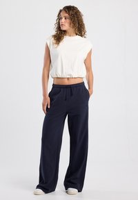 White cropped top with a round neckline and gathered hem paired with navy wide-leg pants, featuring an elastic waistband and side pockets.