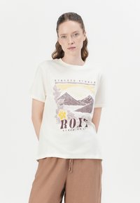 Krémová bavlnená tričko s krátkymi rukávmi, so zobrazením hory, kvetinovými akcentmi a textom "ROXY SINCE 1990" v tmavohnedej farbe.