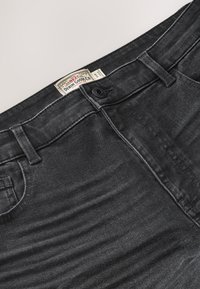Schwarze Denim-Jeans mit Bund, Knopfverschluss, Gürtelschlaufen, Vordertasche und einem Markenstoffetikett auf der Innenseite des Bundes.