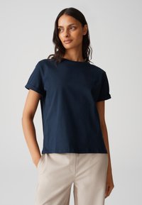 T-shirt in cotone blu navy con maniche arrotolate e colletto a giro; dettaglio logo discreto sul petto sinistro; abbinato a pantaloni beige chiaro.