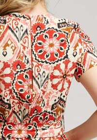 Robe à manches courtes ornée d'un motif floral et géométrique en rouge, rose et noir sur fond crème, avec une fermeture à boutons dans le dos.