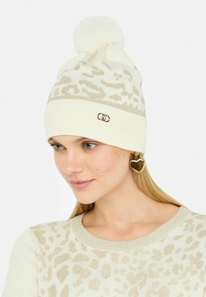 Witte gebreide muts met een leopardprintontwerp in beige en een zachte pompon bovenop. Met een gouden accentlogo op de boord.