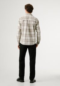 Langärmliges kariertes Hemd in Beige- und Grautönen, mit einem Button-down-Kragen und taillierter Passform, kombiniert mit schwarzen Hosen und Schuhen.