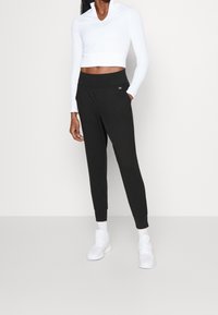 Czarne zwężane spodnie dresowe z bocznymi kieszeniami, w zestawie z białą, krótką bluzą na zamek z długim rękawem. Buty sportowe białe z fakturowaną podeszwą.