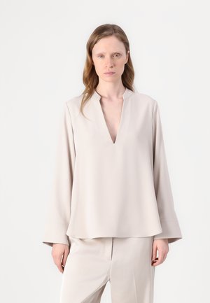 Beige blouse met lange mouwen en een V-hals, met een relaxte pasvorm en een soepele textuur. Draagt een bijpassende broek. Minimalistisch ontwerp.