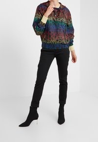 Giacca leggera con motivo arcobaleno, dotata di cappuccio, polsini elasticizzati e dalla vestibilità rilassata, abbinata a pantaloni neri su misura e stivaletti con tacco.