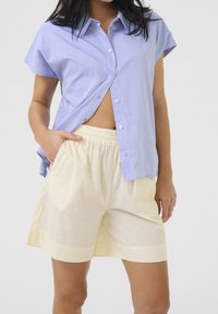 Jasnoniebieska koszula z krótkim rękawem na guziki o luźnym kroju i kołnierzyku, w zestawie z kremowymi, plisowanymi szortami na elastycznej talii.