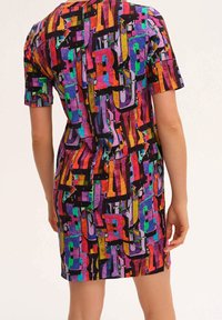 Kurzärmeliges Kleid mit einem bunten abstrakten Muster aus großen Buchstaben in lebendigen Rot-, Lila-, Grün- und Blautönen auf schwarzem Hintergrund.