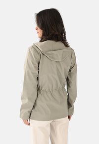 Chaqueta impermeable ligera de color verde oliva con capucha, cintura elástica y mangas largas, con textura suave y diseño minimalista.