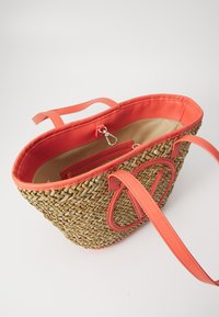 Πλέκητο καλάθι από καλάμι με κοραλλί συνθετικό δέρμα στις λεπτομέρειες και τις λαβές. Το εσωτερικό έχει μπεζ επένδυση με τσέπη που κλείνει με φερμουάρ και κλιπ.