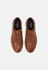 Hnědé kožené boty s hladkým povrchem, které mají šedé tkaničky, nízký profil a výrazné prošívání na stranách.