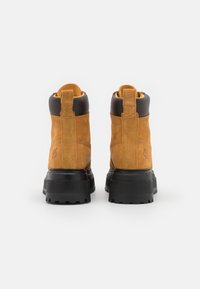 Stivaletti in suede marrone con suola e tacco in gomma nera, dotati di un tassello per il pull e di un logo impresso sul lato.