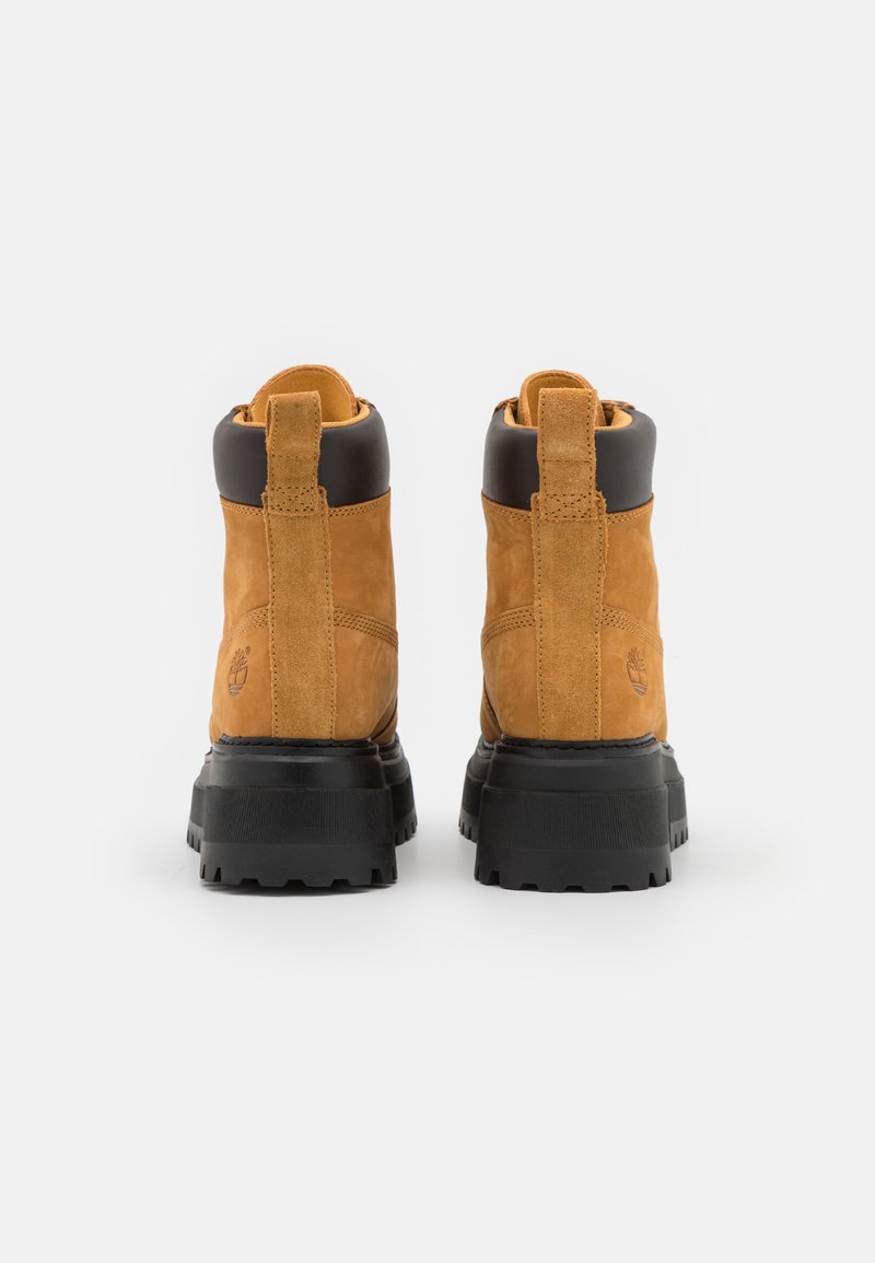 Stivaletti in suede marrone con suola e tacco in gomma nera, dotati di un tassello per il pull e di un logo impresso sul lato.