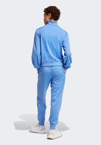 Svijetloplavi trenirku s visokim ovratnikom, dugim rukavima i elastičnim manžetama, uparen s pripadajućim hlačama. Materijal izgleda glatko i rastezljivo.