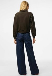 Avskuren olivgrön sweatshirt med hög krage, i kombination med högmidjade, vida mörkblå jeans. Slät textur och minimal detaljering.