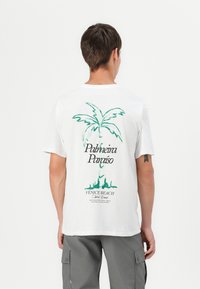 Balto medvilninio marškinėliai su žaliu palmės medžio grafika ir tekstu ant nugaros, kur yra "Palmeira Paraíso" ir "Venice Beach".