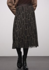 Transparante zwarte midirok met geometrisch patroon in donkergrijs, geplooid ontwerp, elastische tailleband, gedragen met zwarte enkellaarsjes.