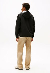Giacca leggera nera con cappuccio, orlo elastico e maniche lunghe. Abbinata a pantaloni beige a gamba larga e sneakers bianche.