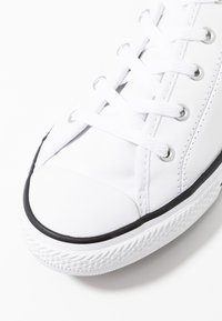 Hvit lær sneaker med rund tå, svart gummiyttersåle og hvite snørebånd. Har sølvfargede hull og teksturert sidepanel.