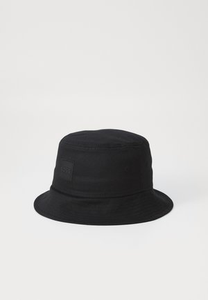 Czarny kapelusz typu bucket z materiału, z okrągłą koroną i szerokim rondem, oraz kwadratową łatką logo z przodu. Brak widocznych wzorów lub ozdób.