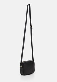 Černá kožená crossbody taška čtvercového tvaru, s texturovaným povrchem, nastavitelným popruhem a zlatými akcenty. Zipové uzavření nahoře.