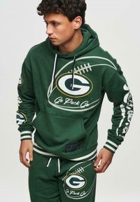 Sweat-shirt vert avec capuche et poche avant, présentant des graphiques de football blancs et le logo de l'équipe. Rayures sur les manches et la ceinture. Matériau en mélange de coton.