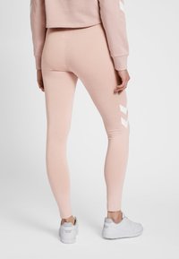 Różowe legginsy wykonane z miękkiego, elastycznego materiału, z białym wzorem typu jodełka na dolnych bokach, zestawione z białymi sneakersami.