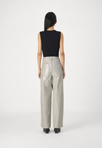 Μαύρο χωρίς μανίκια τοπ συνδυασμένο με ψηλόμεσα, ανοιχτό γκρι, γυαλιστερά παντελόνια σε κροκό σχέδιο με απλή υφή και ορατές ραφές.