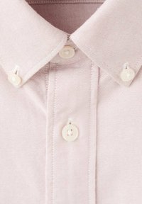 Camisa rosa claro con cuello, confeccionada en tejido texturizado, con dos botones en el cuello y un patrón de tejido sutil. Detalles en costuras blancas.