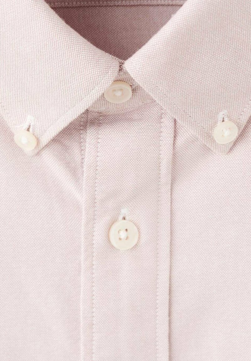 Camicia rosa chiaro con colletto, realizzata in tessuto texturizzato, con due bottoni sul colletto e un motivo a trame sottili. Dettagli con cuciture bianche.