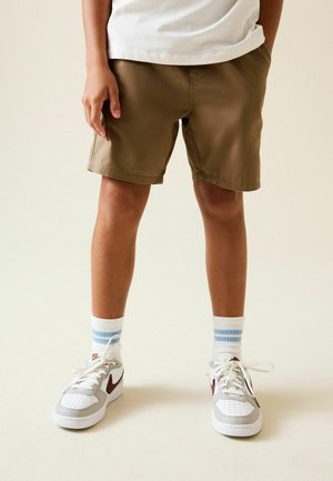 Khaki-colored shorts made of fabric, with a relaxed fit and hem ending above the knee. Paired with white sneakers and blue-striped socks.