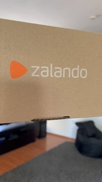 Pruun kartongkast, millel on sile pind; vasakul küljel on trükitud "zalando" valge värviga ja oranž kolmnurkne logo.