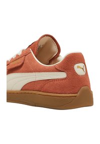 Sneaker in suede arancione con striscia in pelle bianca, suola in gomma e design con lacci. Presenta un piccolo logo sul tallone.