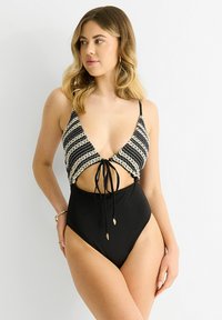 Black and white striped swimsuit with a deep V-neck, open sides, adjustable ties, and a high-cut leg. Made from smooth fabric.