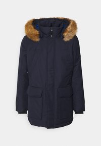 Námořnická modrá zimní parka s předním zipem, velkými klopovými kapsami a kapucí podšitou kožešinou na jednoduchém pozadí.