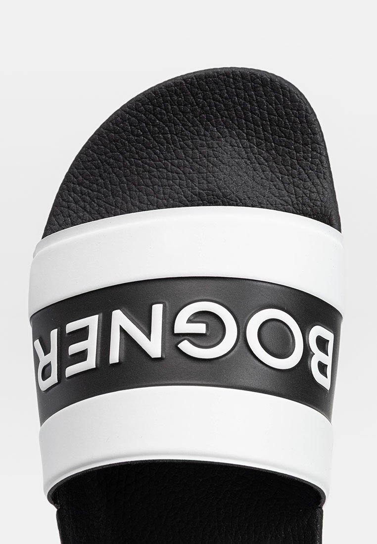 Schwarzer Slide-Sandale mit strukturiertem Obermaterial, versehen mit einem auffälligen weißen Logoband. Die Sohle ist flach mit einem leichten Bogen. Leichtes Design.